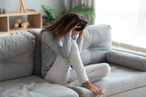 woman sits on couch contemplating the common anxiety triggers